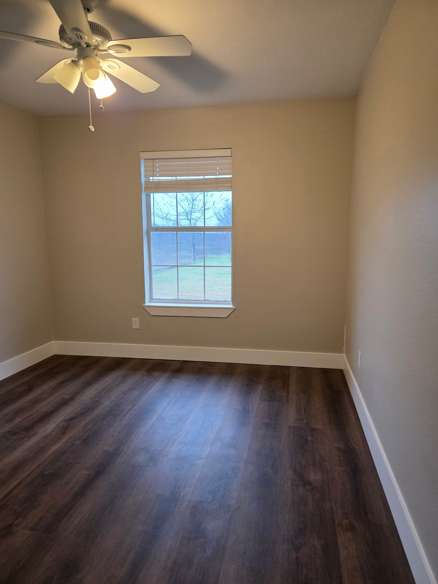 A clean, fully restored residential bedroom featuring new dark wood-style laminate flooring, freshly painted beige walls, and white baseboards after professional restoration services.