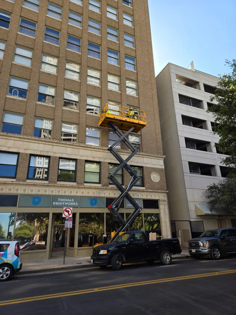 Professional commercial building restoration services with specialized equipment and scissor lift in urban setting