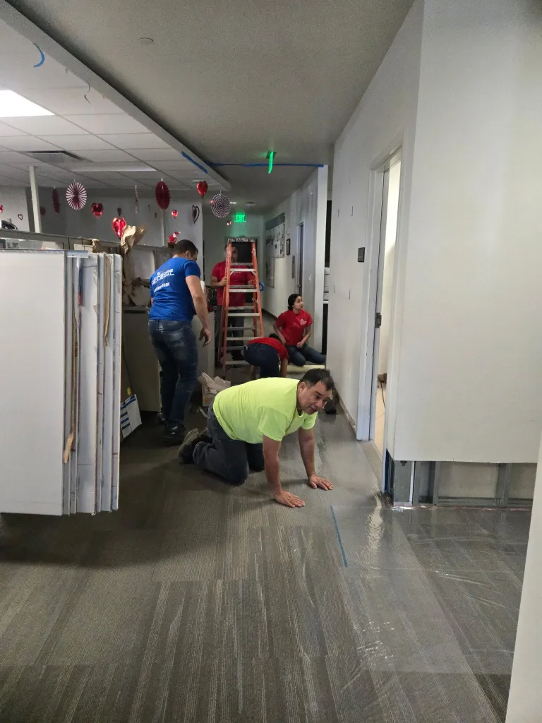 Professional restoration team installing clear plastic floor protection and assessing water damage in a commercial office hallway during a repair project.